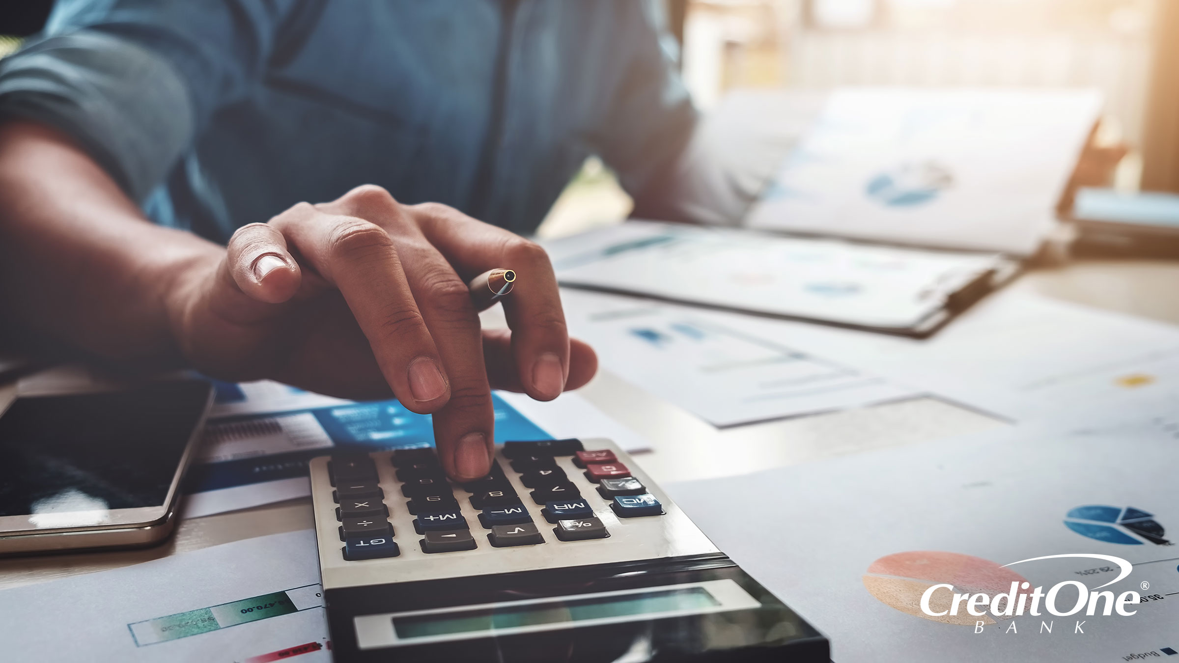 A man uses a calculator while examining reports, possibly checking the rates between a high-yield savings account and a money market account.