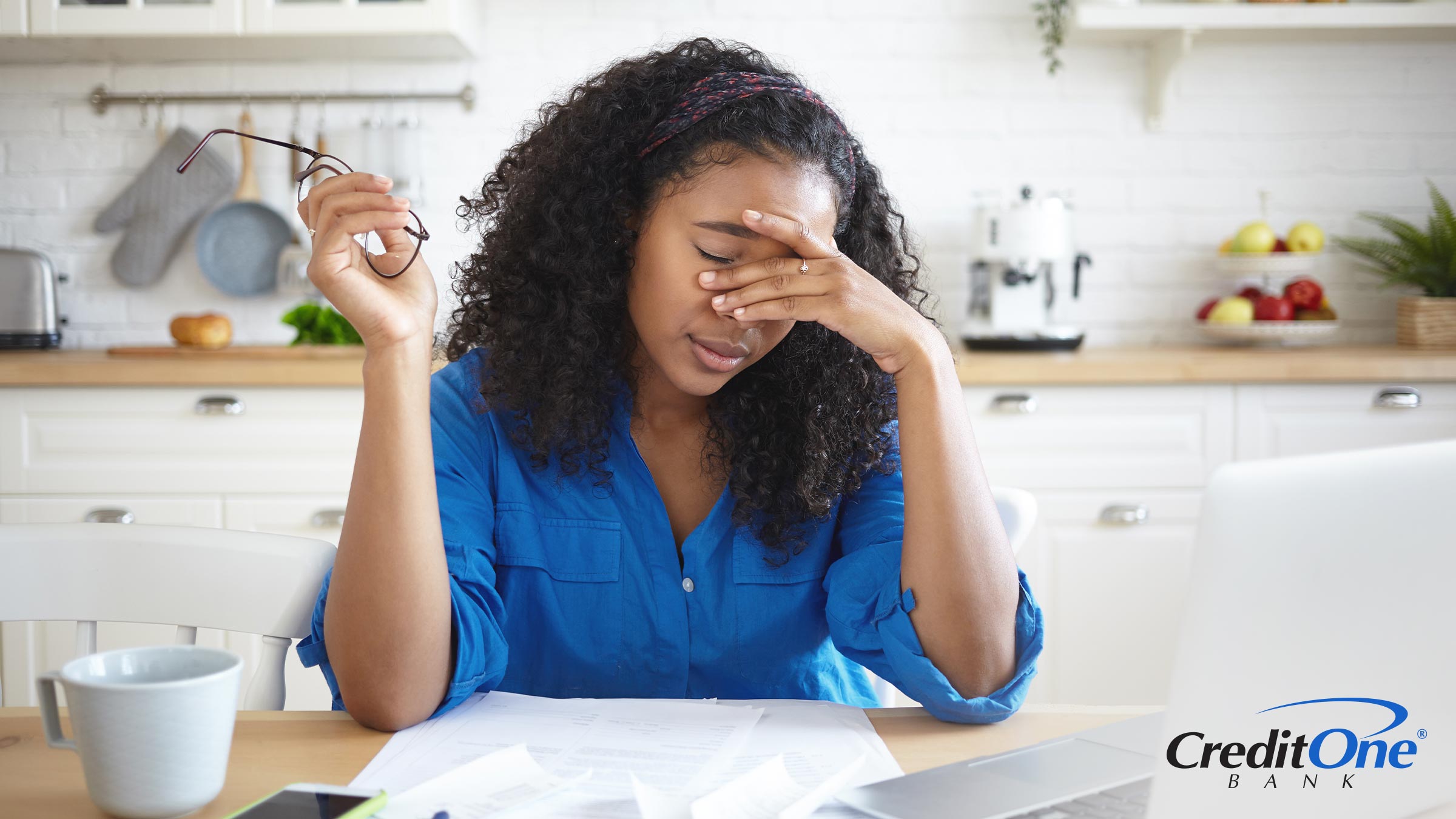 A woman sits at a table, her head resting in her hands, conveying a sense of stress or deep contemplation as to how she can repair her damaged credit.